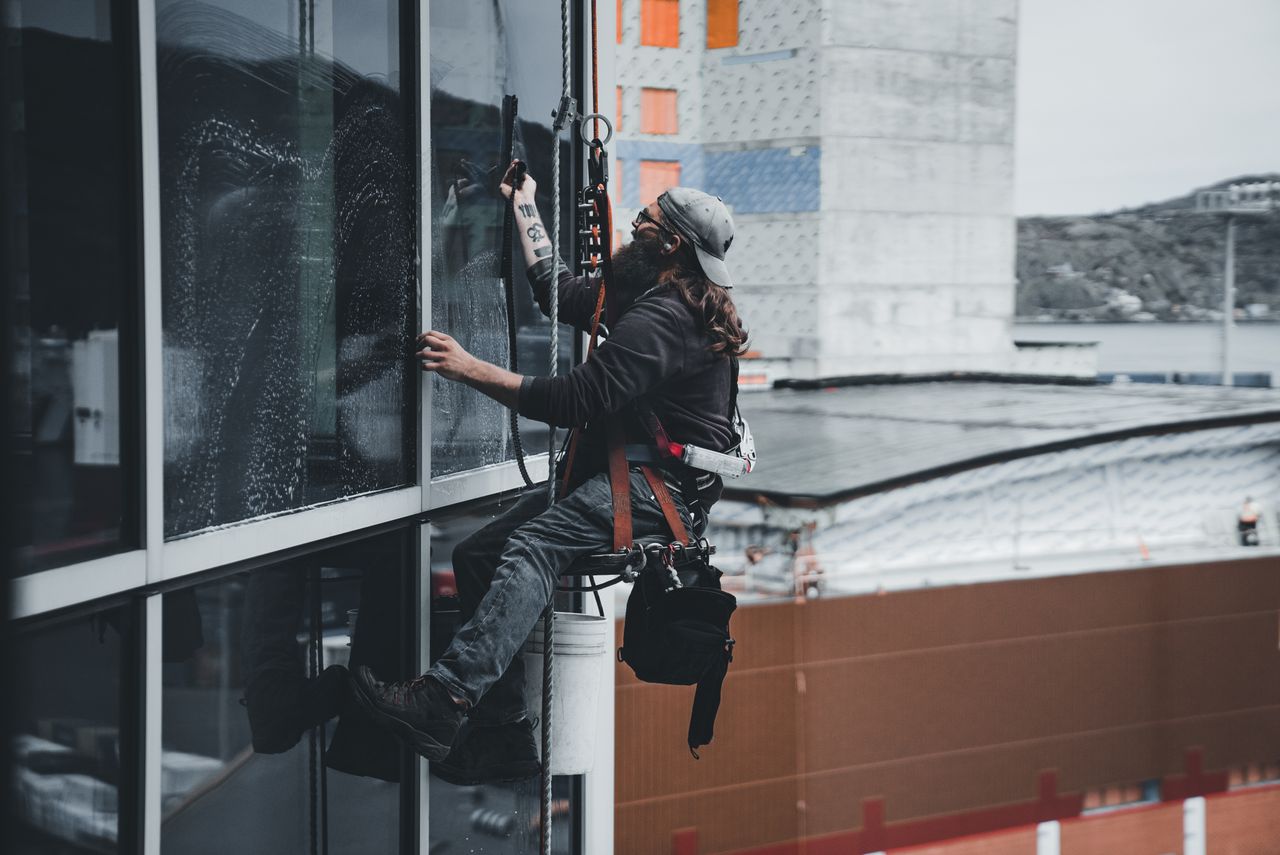 Un homme nettoyant les vitres d’un gratte-ciel avec un harnais, mettant en scène un travail urbain en hauteur.